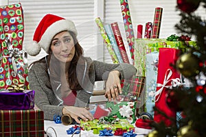 Woman wrapping Christmas presents, looking exhausted.