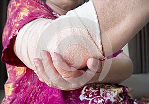 Woman wrapping compression bandage around painful elbow to relieve pain or prevent injury