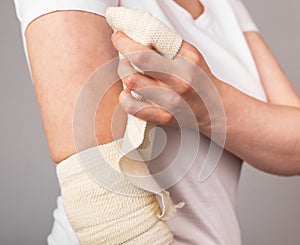 Woman wrapping elastic bandage around painful elbow. Compression wrap. Arm injury, overuse, inflammation, arthritis