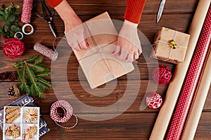 Woman wrapping gift box with decorating items on wood table, close up, top view.