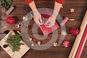 Woman wrapping gift box with decorating items on wood table, close up, top view.