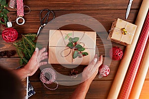 Woman wrapping gift box with decorating items on wood table, close up, top view.