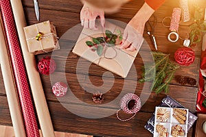 Woman wrapping gift box with decorating items on wood table, close up, top view.