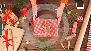 Woman wrapping gift box with decorating items on wood table, close up, top view.