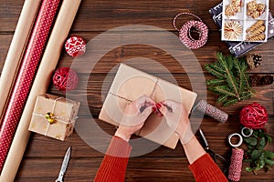 Woman wrapping gift box with decorating items on wood table, close up, top view.