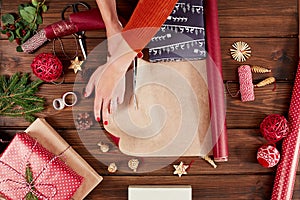 Woman wrapping gift box with decorating items on wood table, close up, top view.