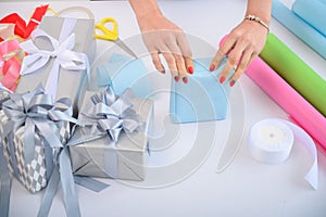 A woman wraps Christmas presents in wrapping paper and ties a ribbon bow. Close-up of woman`s hands preparing surprises