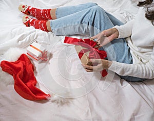 Woman wraps ecological Christmas gifts in wrapping paper, satin ribbon, sitting in a white bed with Christmas