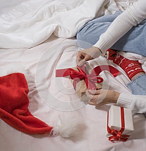 Woman wraps ecological Christmas gifts in wrapping paper, satin ribbon, sitting in a white bed with Christmas