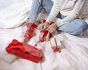 Woman wraps ecological Christmas gifts in wrapping paper, satin ribbon, sitting in a white bed with Christmas