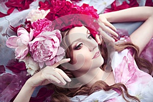 Woman in a wreath of peonies lies among petals