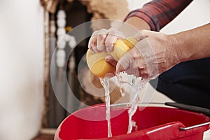 Woman wringing water out of a sponge into a bucket, detail photo