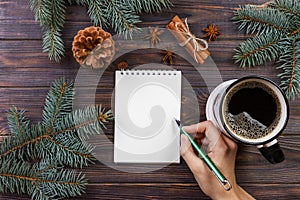 Woman write wishes or to do list in notebook, coffee mug, Christmas. christmas tree branches, pine cones, red berries, on marble t