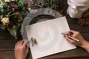 Woman writes in an empty notebook. The table is decorated with dried flowers and a skull.