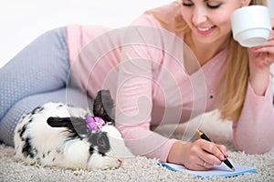 Woman writes a letter in a romantic home atmosphere, lying on the carpet with a rabbit.