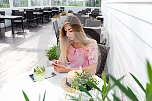 A woman writes a message in phone, in summer in a cafe, a pink dress, rest in a restaurant. Breakfast lunch on summer