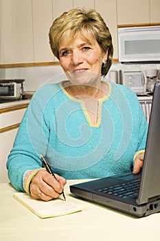 Woman writes a note while using a laptop.