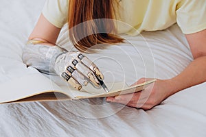 Woman writes in paper notebook with bionic arm lying on bed