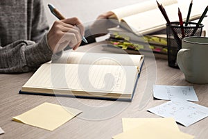 Woman writing ad text.Woman as a copywriter.Closeup of desk and stack of books,notebook,stationary,papers on it