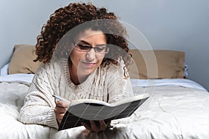 Woman writing on bed at home