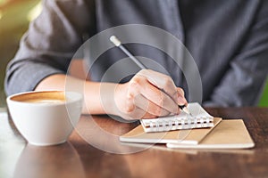 A woman writing on blank notebook with coffee cup on table in cafe