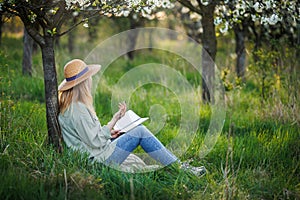 Woman is writing diary and resting in blooming orchard