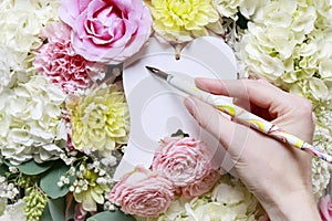 Woman writing greetings on white angel`s wings. Romantic flower ornament