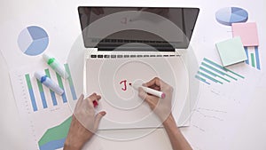 Woman writing JOB on a piece of paper on laptop. Business desktop with diagrams.