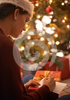 Woman, writing letter and Christmas in home by tree, present and santa hat with message for festive wish. Girl, person