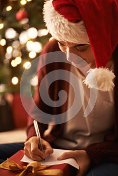 Woman, writing letter and Christmas with smile by tree, present or santa hat with message for festive wish. Girl, person