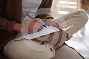 Woman writing letter while sitting on sofa at home, closeup