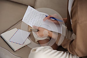 Woman writing letter while sitting on sofa at home, closeup