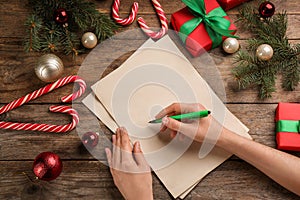 Woman writing letter to Santa Claus at wooden table, top view. Christmas celebration