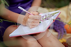 Woman writing in notebook with bouquet of wildflowers - lupines. Closeness to nature, self-discovery concept. Close up