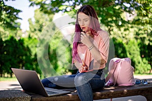 Woman writing in a notebook sitting on a wooden bench in the park. Girl working outdoors on portable computer, copy