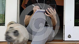 Woman writing on notepad and using cellphone. Home setting, with pug dog.