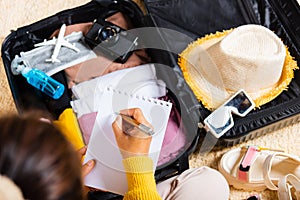 Woman writing paper take note and packing suitcase to vacation writing paper list sitting on room