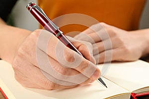 Woman writing with pen in notebook at table, closeup of hands