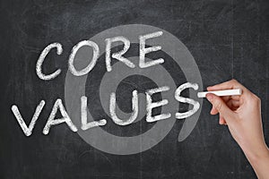 Woman writing phrase CORE VALUES on blackboard