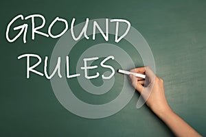 Woman writing phrase GROUND RULES on chalkboard