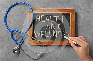 Woman writing phrase Health and wellness on blackboard