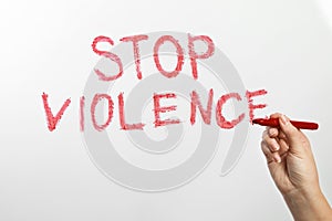 Woman writing phrase STOP VIOLENCE on glass against white background