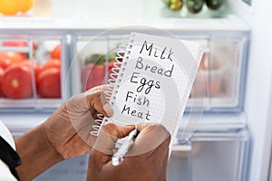 Woman Writing On Shopping List Near Refrigerator