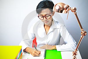 Woman writing in spiral notepad placed on bright desktop.