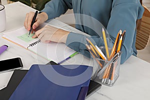 Woman writing on sticky note at white marble table indoors, closeup