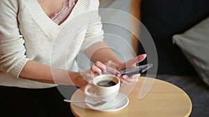Woman writing at the table, drinking coffee or tea. She stirring a cup and looking at smartphone. Closeup