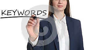 Woman writing word KEYWORDS on transparent board against background, closeup