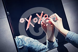Woman writing xoxo on a mirror with red lipstick. photo
