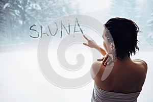 Woman wrote `sauna` word on misted window in welness zone