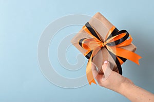 A woman& x27;s hand holds a gift box with a black-orange ribbon on a blue background.
